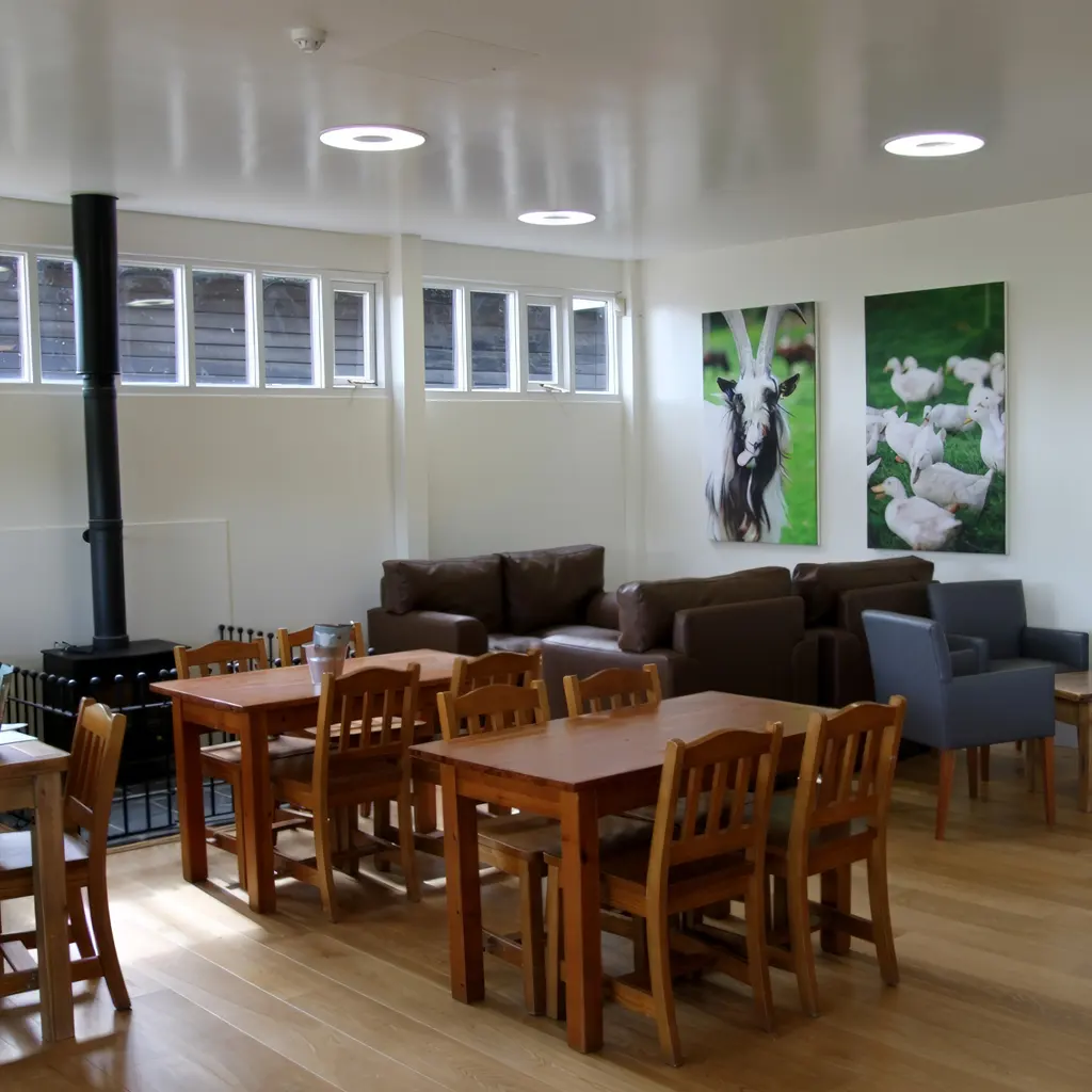 A lounge area in Essex with wooden tables and chairs, brown sofas, a wood-burning stove, and animal-themed wall art on a white wall—perfectly designed by an architect for comfort and style.