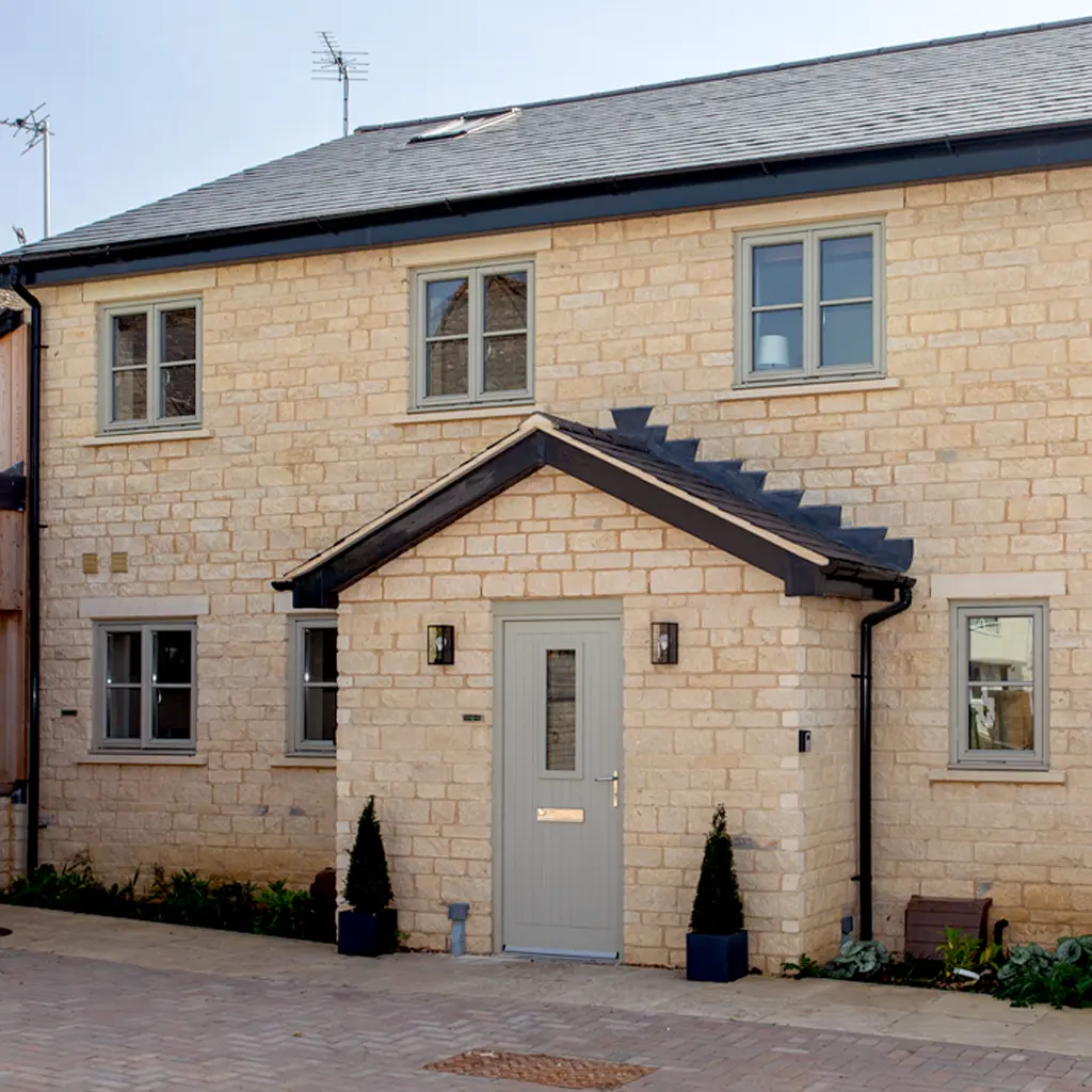 A two-story house with light-colored brick exterior, a small covered entrance, grey door, and multiple windows set on a paved area—designed by an Essex architect with careful attention to party wall considerations.