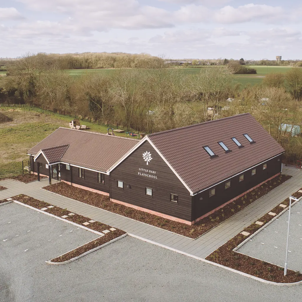 Aerial view of a single-story, modern dark wood building with a tile roof, labeled "Rettendon Primary School," designed by an Essex architect, surrounded by parking and countryside.