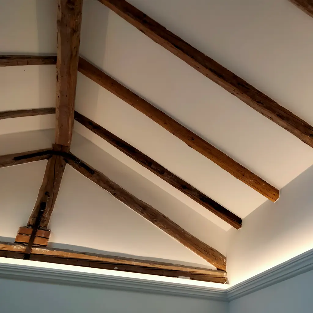 Exposed wooden beams on a white slanted ceiling with a light blue-gray wall and crown molding, designed by an Essex architect.