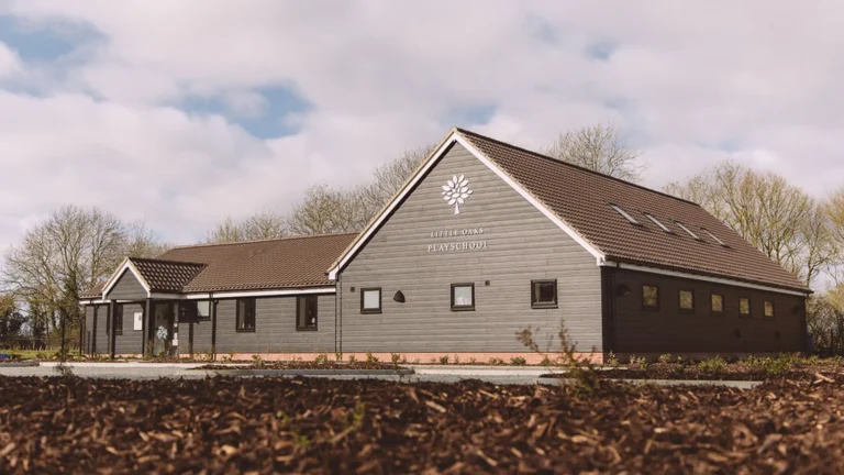 A single-story gray building with a gabled roof and "Littletons Parish Room" sign on the front, set amid trees and mulch. The design reflects classic Essex style, with careful attention to party wall details.