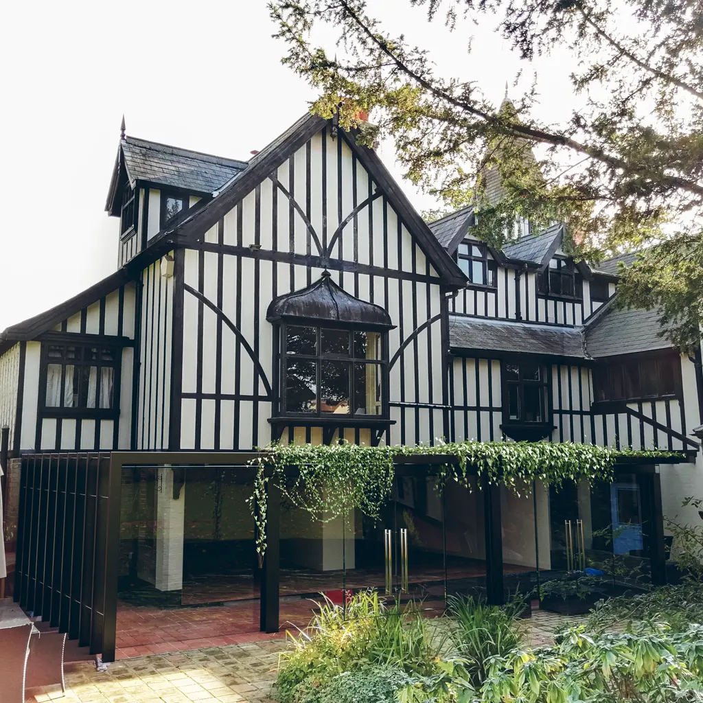 A large Tudor-style house in Essex with black timber framing, white walls, multiple gables, and a modern glass extension covered with hanging plants—expertly designed by an architect to respect party wall guidelines.