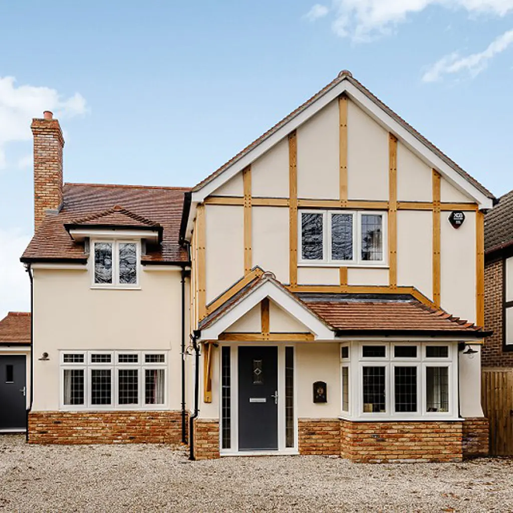 Two-story detached house in Essex with a peaked roof, brick and stucco exterior, gravel driveway, modern gray front door under a small gable, and a party wall designed by an architect.