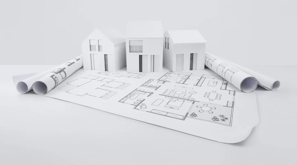 Three white architectural house models sit atop detailed floor plans and blueprints, surrounded by rolled drafts—an ideal scene for an Essex architect planning layouts or addressing party wall considerations.