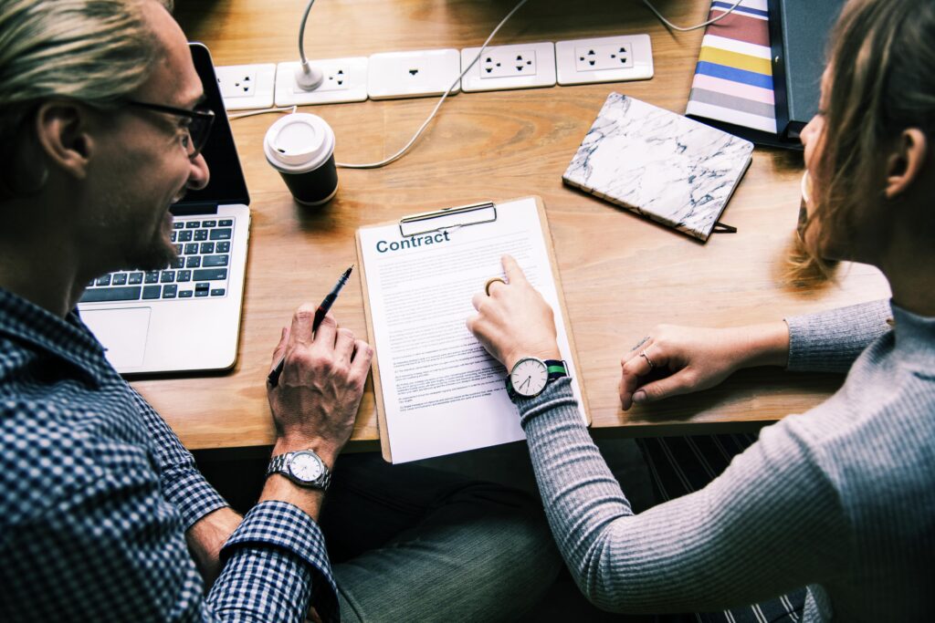 Two people sit at a desk reviewing and discussing a contract document about planning permission in Chelmsford; one person points at the contract while the other holds a pen.
